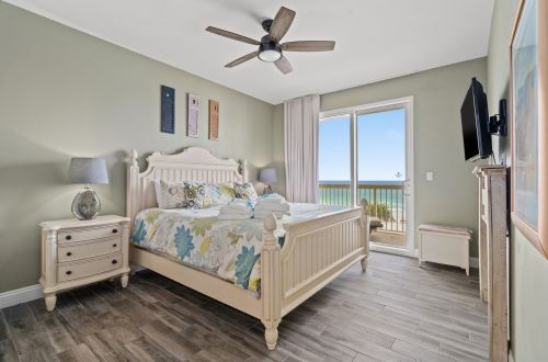 A wide view of a bedroom with a bed, nightstand, TV, and a sliding glass door leading to a balcony.