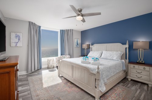 A wide view of a hotel room with a bed, nightstands, and a window with a view of the ocean.