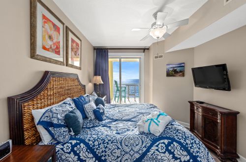 A wide view of a hotel room with a blue and white bed, wicker headboard, and balcony with ocean view.