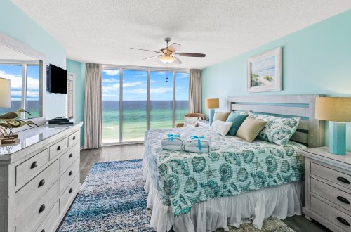 A wide view of a guest room with a bed, dresser, and TV, overlooking the ocean.