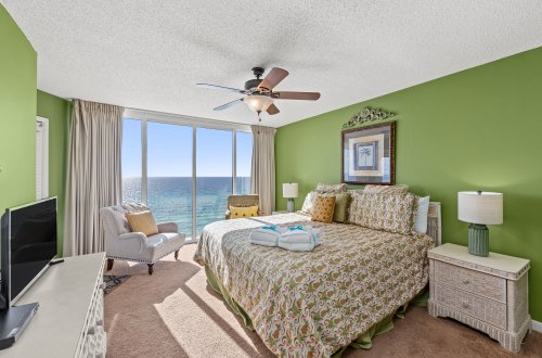 A wide view of a beach-themed guest room with a large bed, TV, and ocean view.