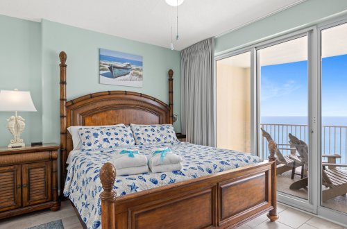 A wide view of a guest room with a large bed, balcony access, and ocean view.