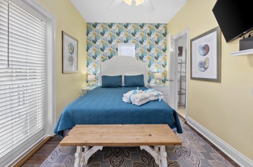 A hotel room with a blue bed, white headboard, and floral wallpaper.