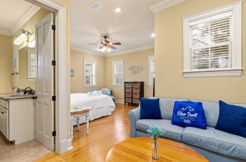 A wide view of a living room with a sofa, coffee table, and open door leading to a bedroom and bathroom.