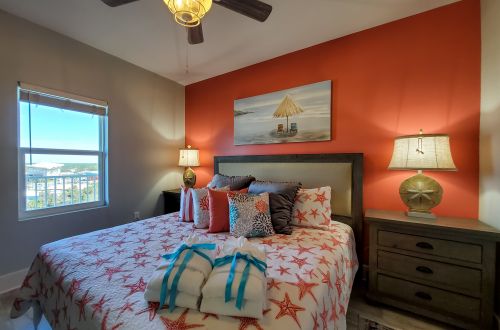 A neatly made bed with starfish patterned bedding and a view from the window.