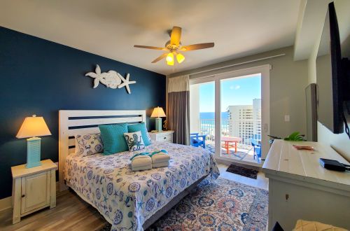 A wide view of a guest room with a double bed, nightstands, a ceiling fan, and an ocean view.