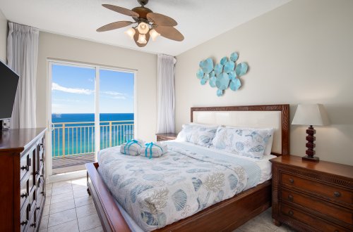 A wide view of a hotel room with a bed, balcony, and ocean view.