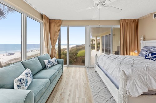 A wide beach room with a sofa, bed, and sliding doors leading to a balcony with a beach view.