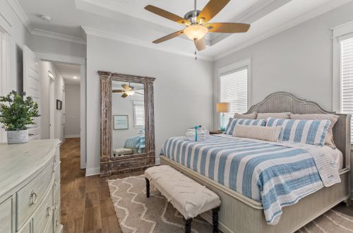 A wide view of a bedroom with a bed, dresser, mirror, and bench.