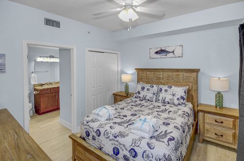 A guest room with a bed, nightstands, lamps, a ceiling fan, and a doorway to the bathroom.