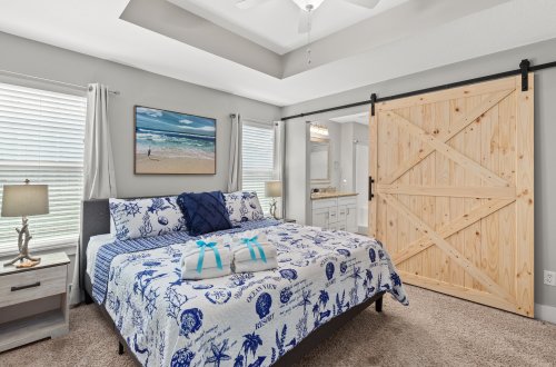 A wide view of a bedroom with a bed, nightstand, and sliding barn door.