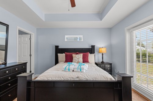 A wide view of a bedroom with a bed, dresser, nightstand, and window.