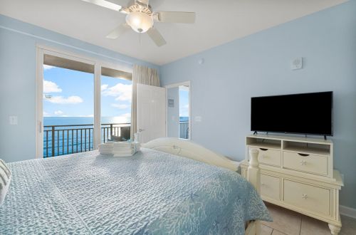 A wide view of a light blue beach room with a bed, TV, and balcony access.