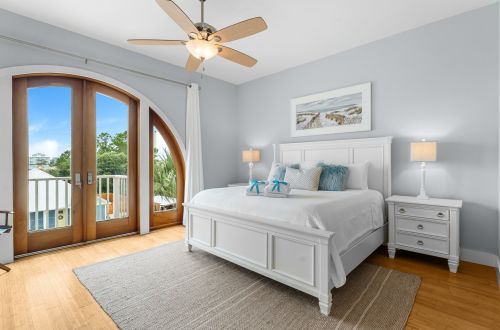 A wide view of a guest room with a white bed, nightstand, ceiling fan, and balcony door.