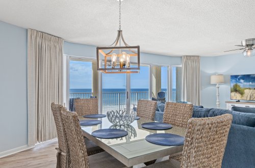 a dining area with a glass table, wicker chairs, and an ocean view