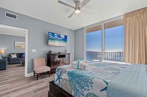 A wide view of a hotel room with a bed, TV, and balcony access showing ocean views.