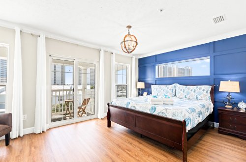 A wide view of a guest room with a large bed, balcony, and wooden floor.