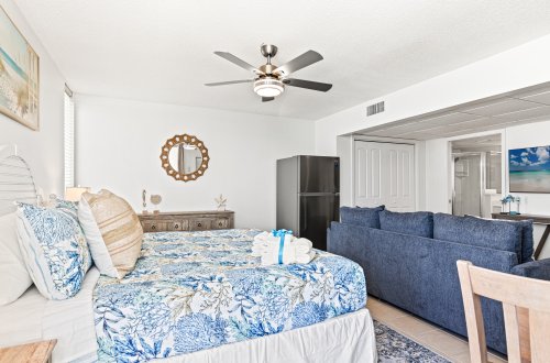 A wide view of a hotel room with a bed, sofa, and refrigerator.