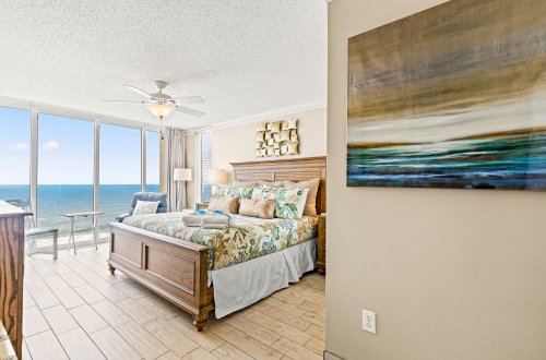 A wide view of a guest room with a bed, chair, and large windows showing the ocean view.