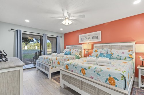 A wide view of a room with two beds, an orange accent wall, and a sliding glass door.