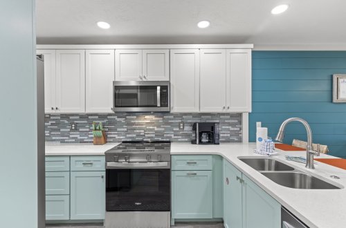 A modern kitchen with white and light blue cabinets, stainless steel appliances, and a gray backsplash.