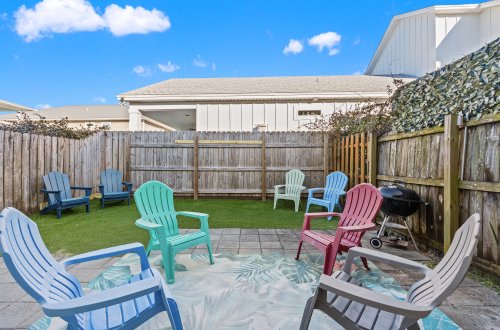 A fenced-in outdoor seating area with Adirondack chairs and a grill.