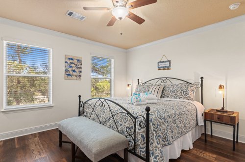 A wide-angle view of a bedroom with a bed, two windows, a bench, and a nightstand.