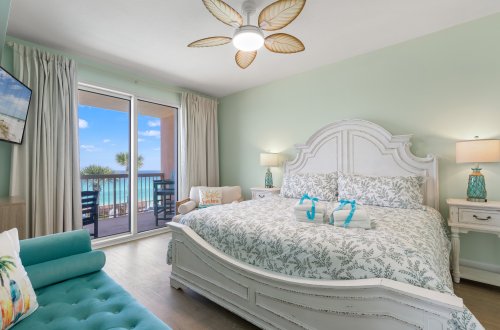A wide view of a bedroom with a large bed, balcony, and sofa.
