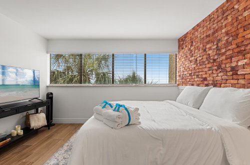 A hotel room with a large bed, white linens, and a brick accent wall.
