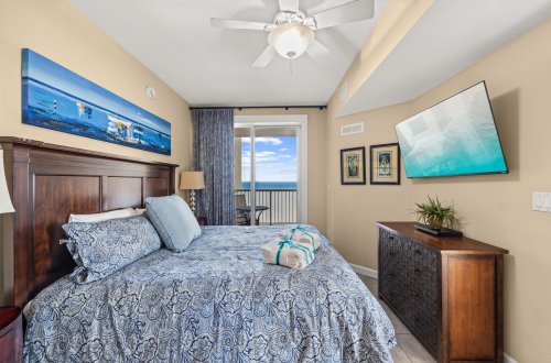 A wide view of a hotel room with a bed, TV, balcony, and artwork.